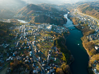 夕日に照らされた紅葉した山々と田舎の町並み　空撮