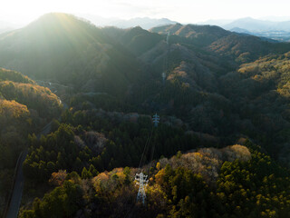 夕日に照らされた紅葉した山々の中に建設された鉄塔・送電線・電線路・高圧線　空撮