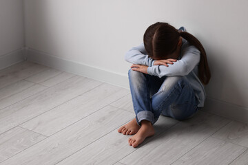 Child abuse. Upset little girl sitting on floor near light wall indoors, space for text