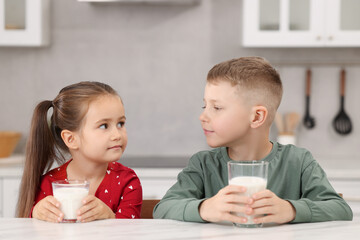 Cute children with glasses of milk at white table in kitchen