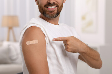 Man pointing at sticking plaster after vaccination on his arm at home, closeup