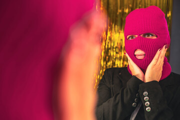 A young woman in a pink balaclava looks in the mirror - obrazy, fototapety, plakaty
