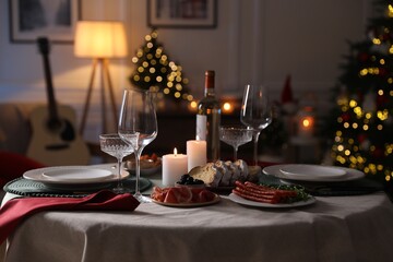 Christmas table setting with burning candles, appetizers and dishware in room