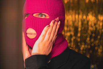 A young woman in a pink balaclava looks in the mirror