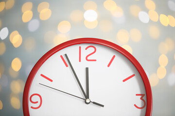 Fototapeta na wymiar Clock showing five minutes until midnight on blurred background, closeup. New Year countdown