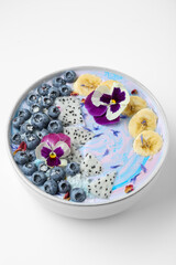 Obraz na płótnie Canvas Delicious smoothie bowl with fresh fruits, blueberries and flowers on white background