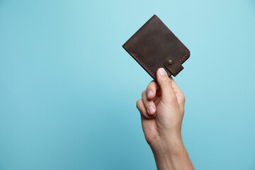 Man holding leather wallet on light blue background, closeup. Space for text
