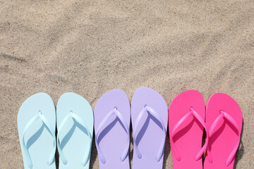 Fototapeta na wymiar Stylish colorful flip flops on sand outdoors, flat lay. Space for text
