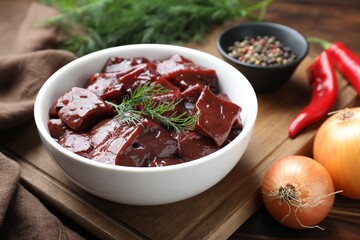 Cut raw beef liver with onions, spices, chili peppers and dill on wooden table
