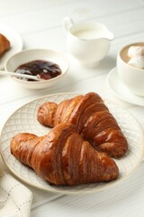 Plate with tasty croissants served on white wooden table, closeup