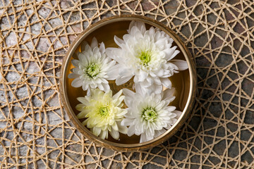 Tibetan singing bowl with water and beautiful chrysanthemum flowers on table, top view