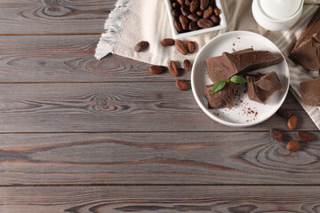 Pieces of tasty milk chocolate, cocoa beans, powder and mint on wooden table, flat lay. Space for...