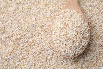 Wooden spoon on raw barley groats, top view. Space for text
