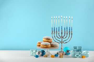 Composition with Hanukkah menorah, dreidels and gift boxes on white table against light blue...