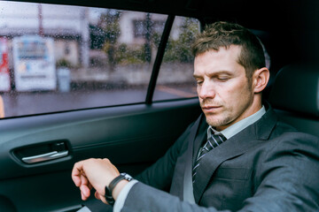 タクシーに乗って腕時計を見る乗客の欧米人ビジネスマン
