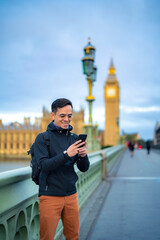 Young Latin male tourist in casual clothes and glasses smiling and standing on bridge near Big Ben...