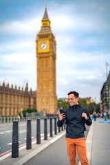Young Latin male tourist in casual clothes and glasses smiling and standing on bridge near Big Ben...