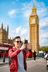 Smiling young Latin male in casual clothes and sunglasses taking selfie on smartphone while...