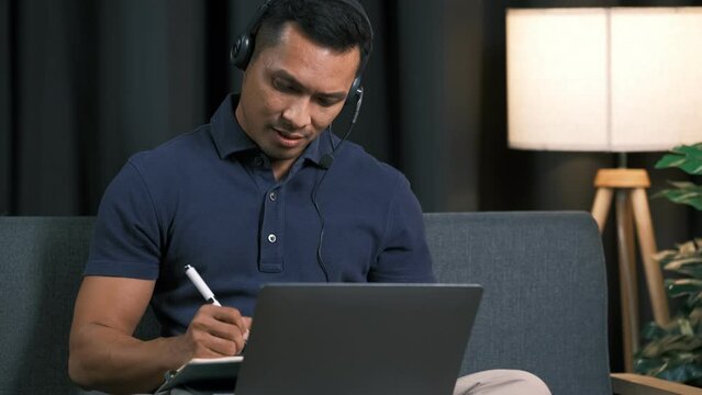 asian people male guy work at home office sofa video call advice on laptop remote telework job online. Young adult hybrid worker man in reskill upskill career class look at webcam digital camera.