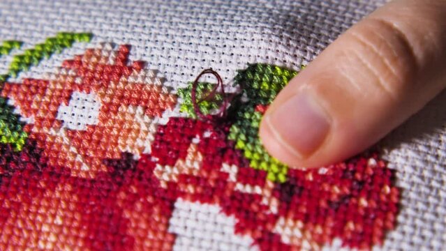 Close-up of a woman's hands busy with cross-stitch embroidery. A beautiful brightly coloured pattern. Relaxing hobby. Process of cross embroidery