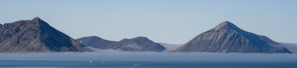 Scenic mountain range rising up out of the Arctic ocean and early morning fog at Gnalodden, Svalbard, peaceful polar nature background
