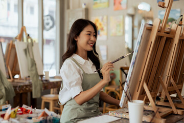 Cheerful young asian woman artist smiling drawing at art studio. © amnaj