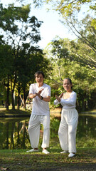 Fototapeta premium Full length view of active retired senior couple practicing traditional Tai Chi outdoors near lake.
