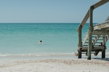 Young Caucasian boy in the water at the sandy beach. Wood walkway on the right side on a bright and sunny day. Blue water and sky in the background. In Florida horizontal shot.