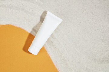 White sand covers a yellow background, a cosmetic tube without a label stands out. Cosmetic mockup for advertising. Skin care with natural cosmetics - safe and benign.