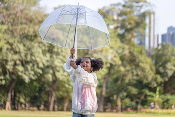 Cheerful child girl with an umbrella playing with rain in the park, Cute little kid girl playing outdoors in the garden