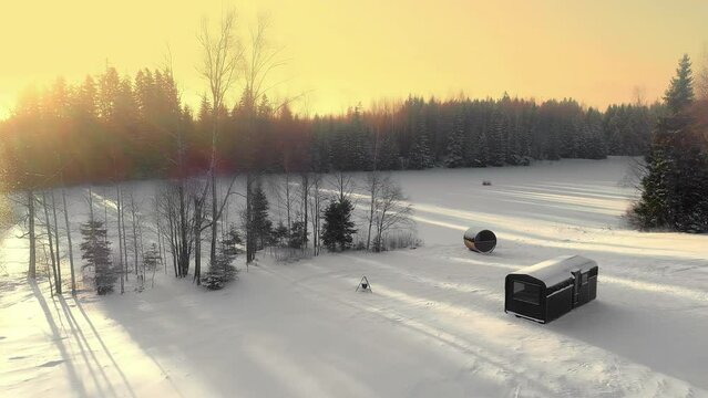 Aerial view flying over a sauna and a cabin at a forest lake, during sunset
