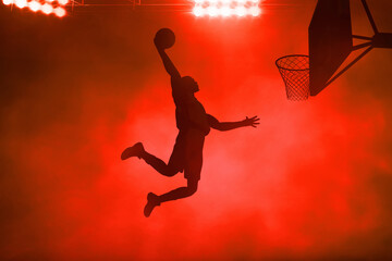 3d illustration shadow silhouette of young professional basketball player slam dunk on dark red smoke background - 692322466