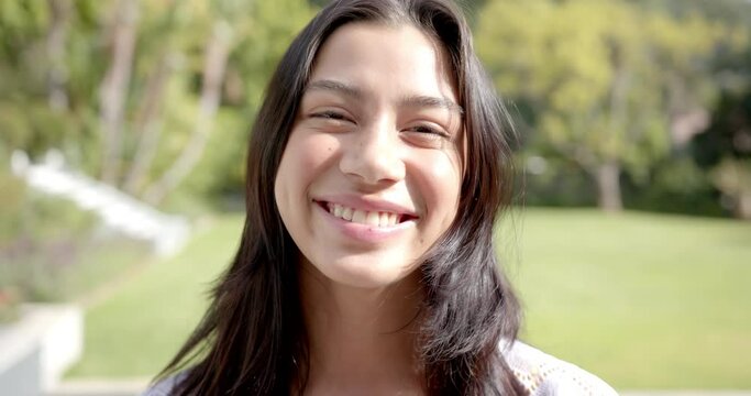 Portrait of happy biracial teenage girl smiling in sunny garden, slow motion