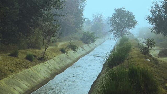 Running water in an irrigation canal through rural India covered with fog on a misty cold morning n Dholpur Rajasthan of India