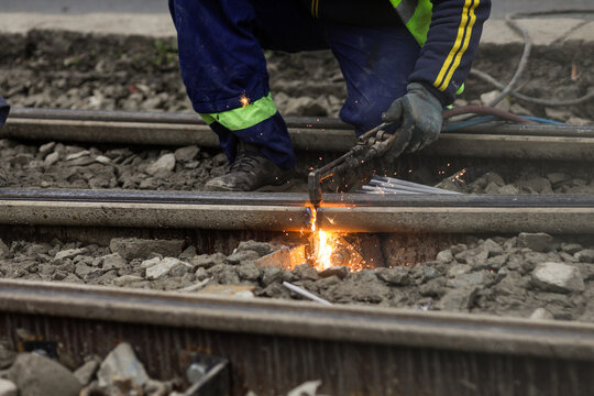Details with a worker using an oxy-acetylene torch to cut metal tramway tracks.