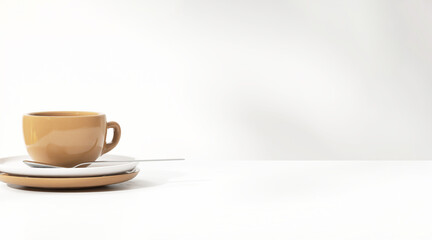 Brown coffee cup and teaspoon on white saucer on table counter in morning sunlight, leaf shadow for...