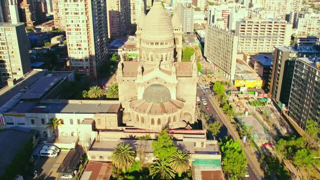 Aerial view establishing tilt up of Los Sacramentinos Church in a residential neighborhood with the mountain range in the background, Santiago, Chile.