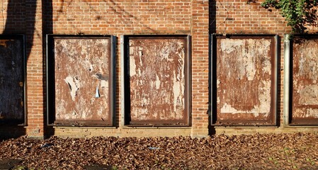Rusty metal boards with scraped street billboards on  brick wall. Sidewalk covered with fallen leaves in front. Grunge background for copy space