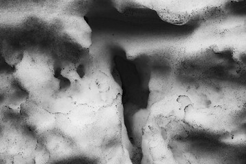 dirty snow in black and white. close-up of a piece of snow with holes. holey snow background in...