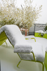 Snow-covered all-season metal furniture with snow-covered table and chairs on a roof terrace