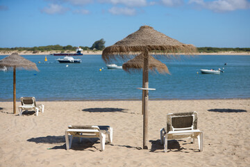 Straw umbrellas and sun loungers on the beach on a sunny day. The concept of rest and relaxation, holidays and travel. In the background the fishermen's boats.