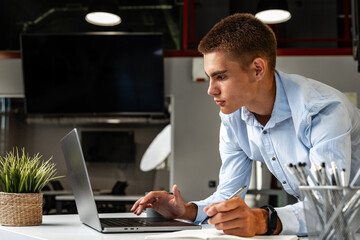 Serious concentrated young entrepreneur working in office on laptop