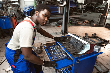 Young african mechanic in uniform working in a car service shop