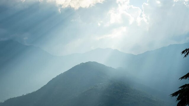 Zoom in 4K time lapse of  sun god rays shining through clouds on mountains in Manali, India. Time lapse of clouds moving over mountains. Dramatic sunrays through the clouds. Sun burst over mountains