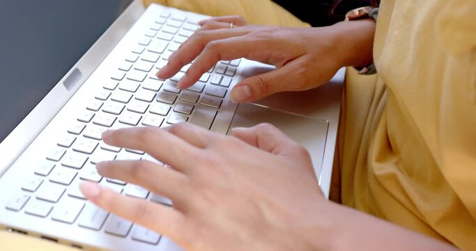 Hands of biracial teenage girl using laptop keyboard, slow motion