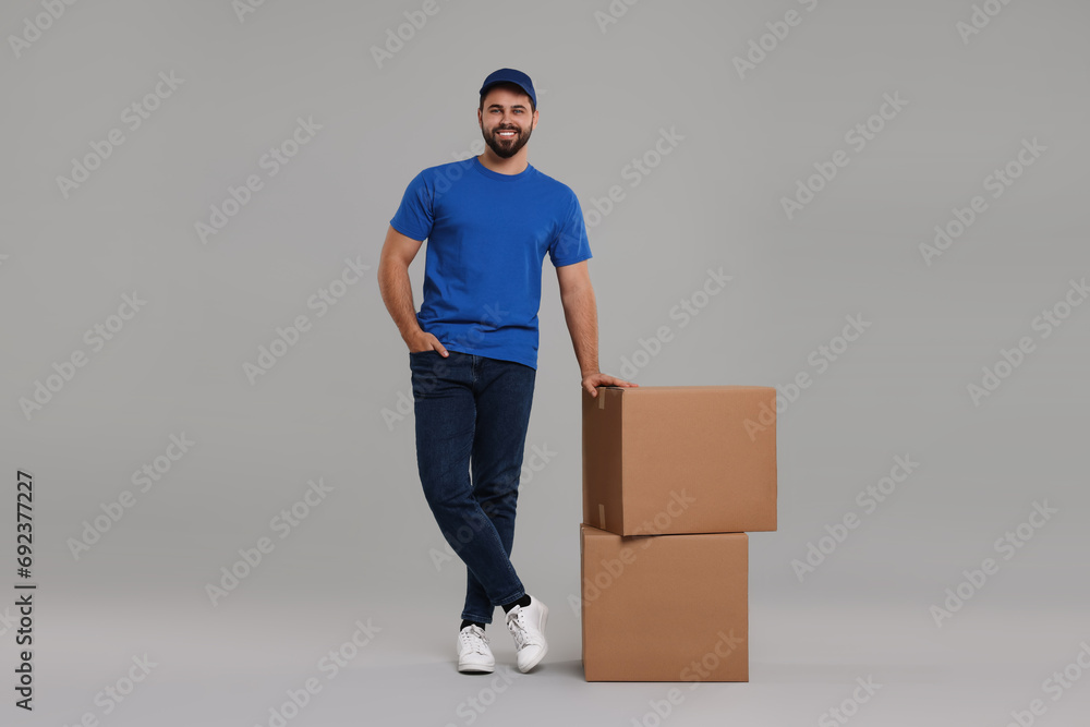 Poster Happy young courier with parcels on grey background