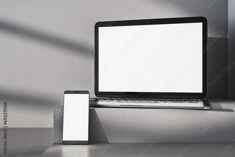 Poster close up of empty white laptop computer and phone on gray desk. concrete wall background, shadows an