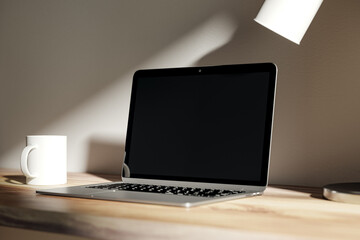Fototapeta premium Modern blurry daytime desktop with blank laptop screen, lamp and coffee cup. Designer workspace concept. 3D Rendering.