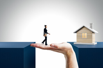 Happy businesswoman walking on hand to reach wooden house through gap on light background. Mortgage...