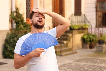 Man with hand fan suffering from heat outdoors